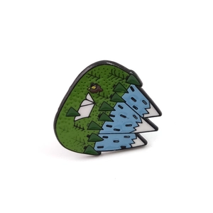 Detailed view of enamel camping brooch featuring green forest and white mountain peaks
