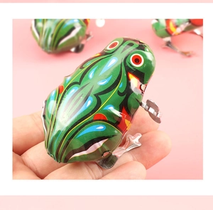 Close-up of a green vintage clockwork tin frog toy held in hand against pink background