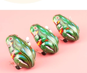 Detailed view of three vintage-style green clockwork wind-up tin frogs on pink background