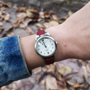 Close-up of bronze cat-ear watch with burgundy leather strap on a wrist outdoors