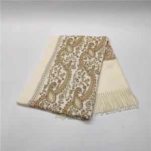 Detailed view of beige cashmere feel scarf with golden paisley embroidery and fringe