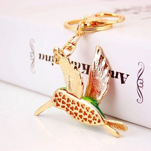 Creative golden hummingbird metal keychain with colorful enamel wings on book background