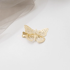 Vue détaillée de la barrette papillon évidée en métal doré sur un fond en maille