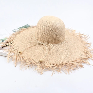 Close-up of beige straw sun hat with frayed edges and wooden adjustment buckle toggle
