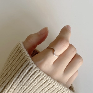 Close-up of minimalist wavy sterling silver ring worn with a warm beige knit sweater