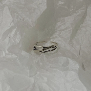 Top view of a minimalist silver crossover woven ring on a textured white paper background