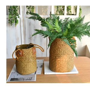 Detail of natural seagrass woven baskets with leather handles and faux ferns on wood table