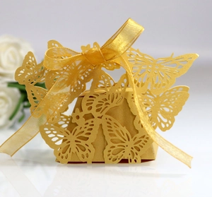 Detailed laser-cut gold butterfly candy box with a satin ribbon and white floral decor