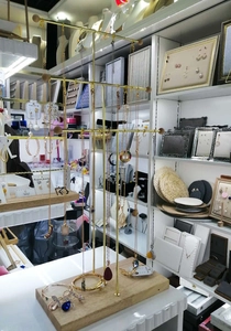 Three-tier gold metal jewelry stand with wooden base displaying multiple necklaces