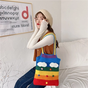 Detail of a handmade rainbow knit bag featuring colorful stripes and plush white clouds
