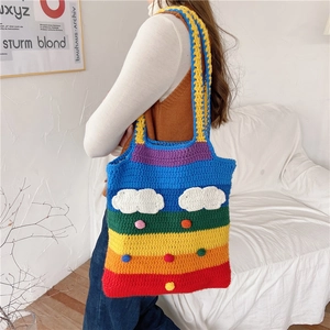 Detail of crochet rainbow striped tote bag with white cloud and colorful pom pom charms