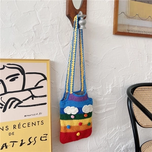 Handmade rainbow crochet tote bag with cloud details hanging on white wall
