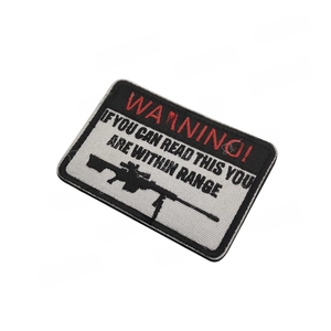 Close-up of rectangular tactical WARNING morale patch with rifle embroidery and velcro backing