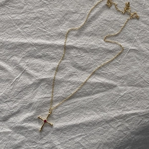 Close-up of gold cross necklace with a central red gemstone on white fabric background