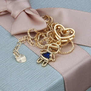 Close-up of gold heart and girl pendant necklace on a blue gift box with pink ribbon