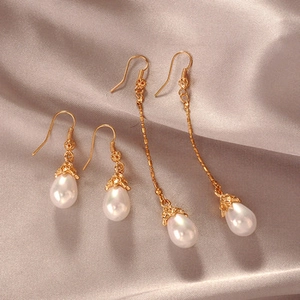 Close-up of golden drop pearl earrings with elegant filigree details on champagne silk