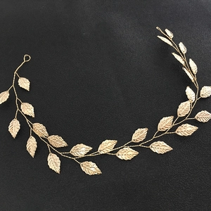 Detailed view of handmade golden metal leaf bridal headband on black textured background