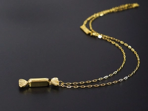 Macro detail of a gold candy-shaped pendant on a fine chain over a black background