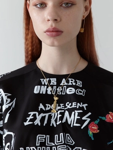 Detail view of gold candy-shaped pendant necklace and safety pin earrings on a model