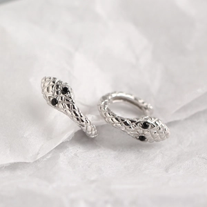Macro shot of silver snake earrings featuring scale textures and black gemstone eyes