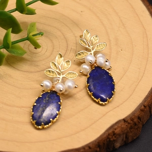 Macro shot of lapis lazuli earrings with white pearls and gold leaf details on wood