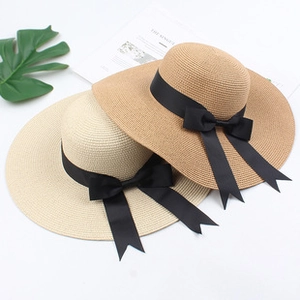 Close-up of straw sun hats with black ribbon bows and green monstera leaf decor