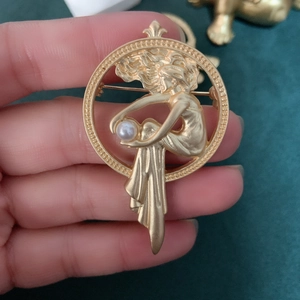 Detailed macro of vintage matte gold brooch featuring an elegant woman and white pearl
