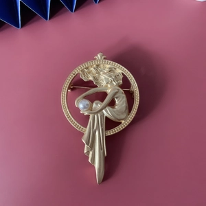 Detailed close-up of matte gold vintage angel brooch with pearl on a pink base