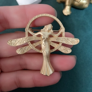 Detailed macro view of matte gold dragonfly goddess brooch with ornate textures