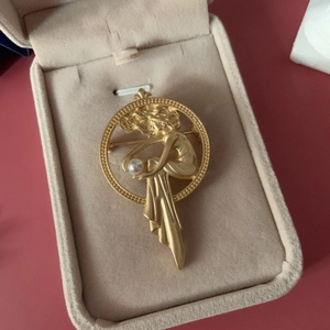 Art Nouveau style matte gold brooch featuring a female figure and a central white pearl