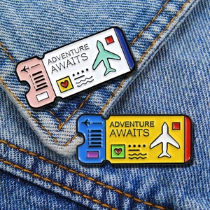 Detail of travel ticket enamel pins featuring Adventure Awaits text on denim fabric