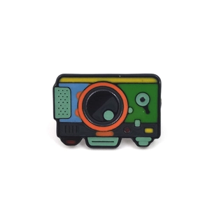 Detail of a colorful vintage camera enamel pin with vibrant forest hiking design