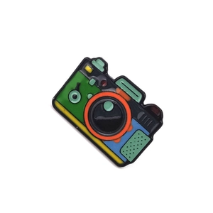 Detailed view of a retro camera enamel pin featuring a colorful forest camping design