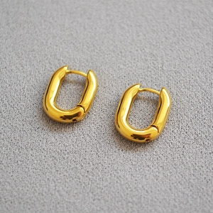 Gros plan de boucles d'oreilles minimalistes dorées en U sur fond de tissu gris texturé