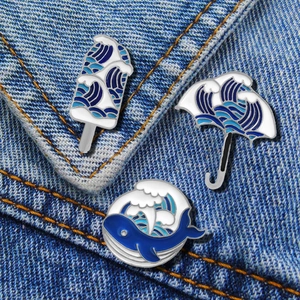 Three enamel wave brooches featuring popsicle, umbrella and whale shapes on denim