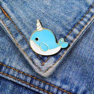 Cute blue enamel narwhal brooch pin with golden plating on denim fabric texture