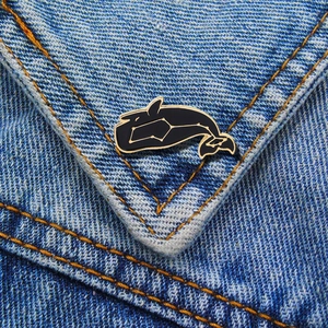 Detail of whale enamel pin with gold constellations on blue denim fabric jacket
