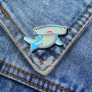 Close-up of blue and green enamel hammerhead shark brooch pin on denim fabric
