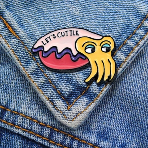 Macro detail of enamel cuttlefish pin with 'LET'S CUTTLE' text on blue denim jacket