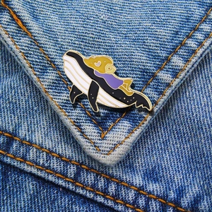Detail of enamel whale brooch with sleeping character pinned on blue denim fabric