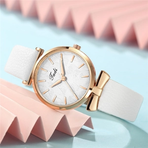 Detail of white leather watch strap with a polished golden bow charm and leaf pattern dial