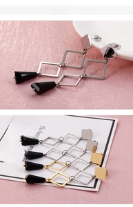 Macro detail of geometric earrings featuring square frames and black faceted trapezoid pendants