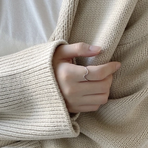 Detailed view of a wave-shaped 925 sterling silver ring on finger with beige knit background