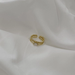 Detail of gold double-layer open ring featuring a rectangular zircon on white fabric