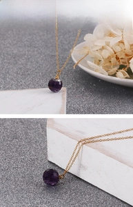 Close-up of golden titanium steel necklace with a faceted purple crystal pendant
