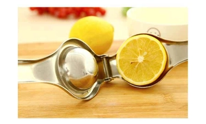 Close-up of stainless steel manual lemon squeezer pressing fresh fruit on wooden board