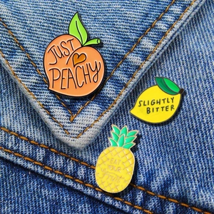 Detailed view of fruit-shaped enamel pins on denim with creative English slogans