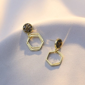 Macro shot of geometric earrings with black rhinestone studs and gold hexagonal pendants