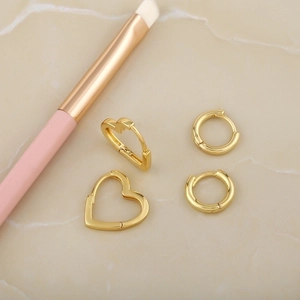 Minimalist gold hoop earring set with heart and round designs on marble surface