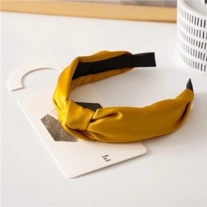 Detailed view of a mustard yellow satin knotted headband on a minimalist white card display